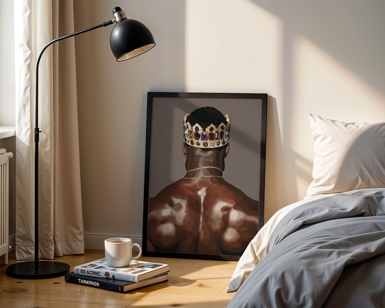 Pode incluir: Uma impress&atilde;o de arte emoldurada retrata uma pessoa usando uma coroa de joias, vista por tr&aacute;s. A obra de arte &eacute; exibida no ch&atilde;o ao lado de uma cama com roupa de cama cinza. Uma lumin&aacute;ria de ch&atilde;o preta e livros com uma x&iacute;cara de caf&eacute; tamb&eacute;m s&atilde;o vis&iacute;veis.