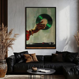 May include: A framed art print featuring a hand holding a green vinyl record above a black turntable. The artwork has a retro aesthetic with a muted color palette, and the hand is adorned with a bracelet. The background is a blend of green and gray.