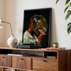 May include: A framed art print depicts a person with a record in place of a head. The artwork is displayed on a wooden cabinet with a record player. A white lamp and a white vase are also on the cabinet.
