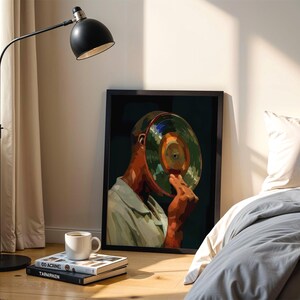 May include: A framed art print depicts a person holding a vinyl record to their face. The artwork features a color palette of green, orange, and brown. A black floor lamp and a white coffee cup on books are in the foreground.
