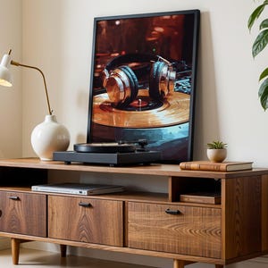 K&ouml;nnte beinhalten: Ein Holz-TV-Schrank mit einem gerahmten Druck von Kopfh&ouml;rern auf einem Plattenspieler. Ein schwarzer Plattenspieler steht oben. Eine wei&szlig;e Lampe und Vase befinden sich links. Eine kleine Pflanze und ein Buch befinden sich rechts.