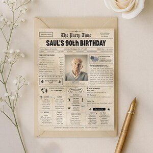 Op de afbeelding: Een verjaardagskaart in vintage-stijl met de kop "SAUL'S 90th BIRTHDAY". De kaart lijkt op een krant, met een foto van Saul, details over 1955 en andere feiten. Een gouden pen ligt ernaast.