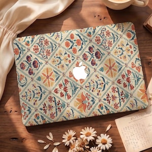 Könnte beinhalten: Eine Laptop-Hülle mit einem Blumenmuster in Orange-, Rot- und Blautönen auf cremefarbenem Hintergrund. Das Design zeigt ein sich wiederholendes Muster aus Blumen und Blättern. Das Apple-Logo ist sichtbar.