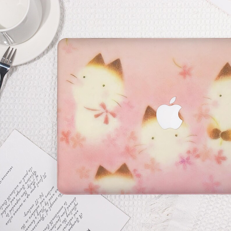 K&ouml;nnte beinhalten: Eine rosa Laptop-H&uuml;lle mit einem sich wiederholenden Muster aus Cartoon-Katzen mit braunen Ohren und rosa Blumendetails. Das Apple-Logo ist sichtbar. Die H&uuml;lle liegt auf einer wei&szlig;en Oberfl&auml;che.