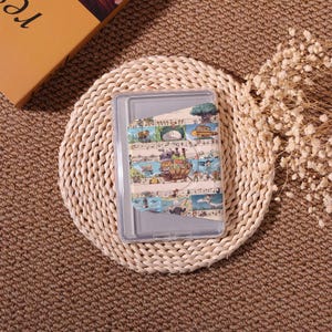 May include: Clear plastic tablet case with a colorful decorative insert featuring illustrations of a fantasy landscape with musical notes. The case is resting on a woven, circular placemat.
