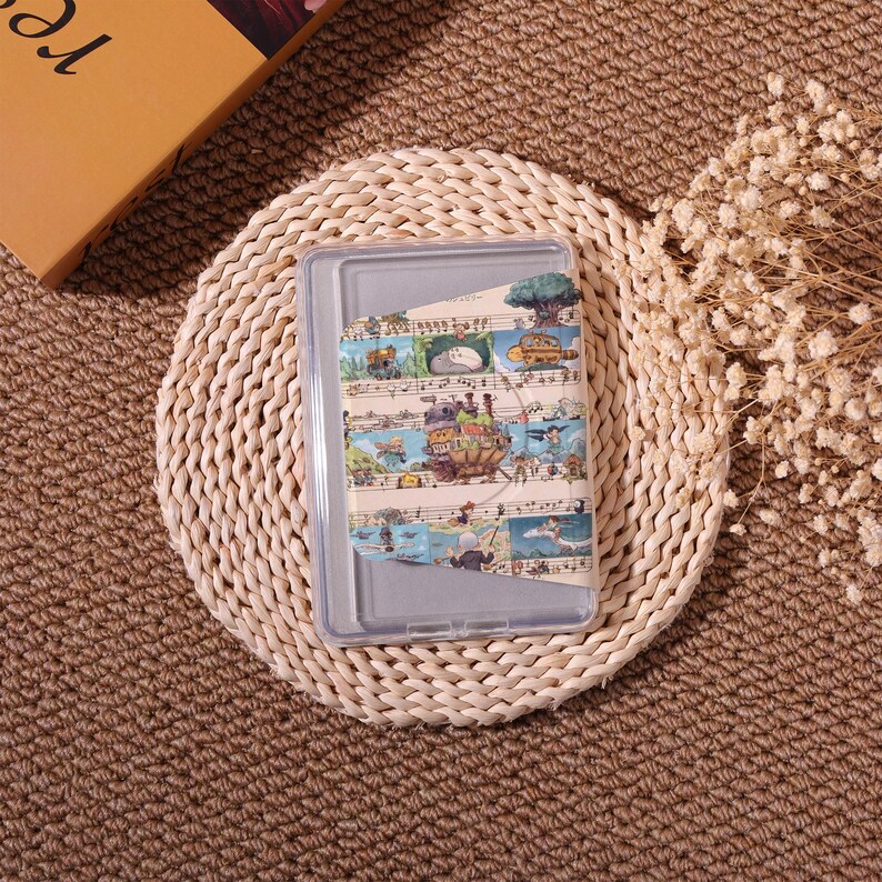May include: Clear plastic tablet case with a colorful decorative insert featuring illustrations of a fantasy landscape with musical notes. The case is resting on a woven, circular placemat.