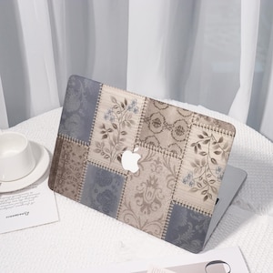 Peut inclure: Coque d'ordinateur portable avec un motif patchwork aux tons beiges, bleus et marron. Motifs floraux et damassés. Le logo Apple est visible. Sur une surface blanche avec une tasse et une soucoupe.