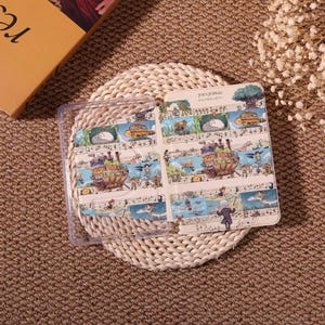 May include: A clear plastic phone case with a colorful, illustrated insert featuring a whimsical musical theme. The insert displays a cartoonish landscape with musical notes and characters, with text in Japanese.