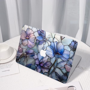May include: A laptop with a floral design. The case features a stained-glass style pattern of blue and purple flowers with green stems and leaves. The Apple logo is visible on the laptop.
