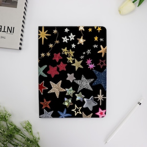 May include: A black notebook cover with a colorful star pattern. The stars are in various sizes and colors, including red, blue, gold, and silver.