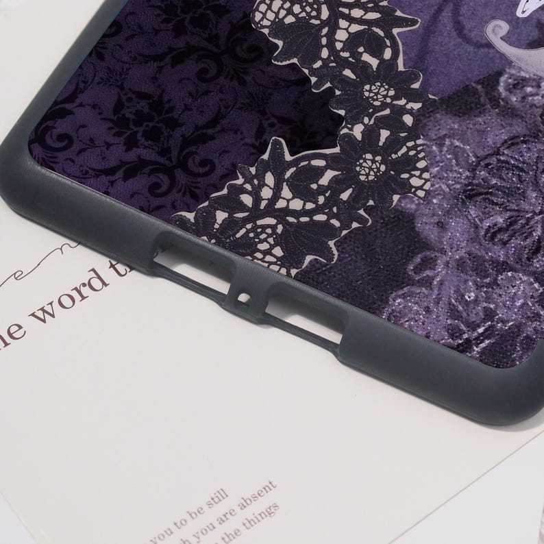 K&ouml;nnte beinhalten: Eine dunkelgraue Handyh&uuml;lle mit einem lila floralen Spitzendesign. Die H&uuml;lle hat einen dunkelgrauen Rand und ein strukturiertes Muster. Das Design umfasst eine Kombination aus floralen und Spitzenmustern in Lila- und Schwarzt&ouml;nen.