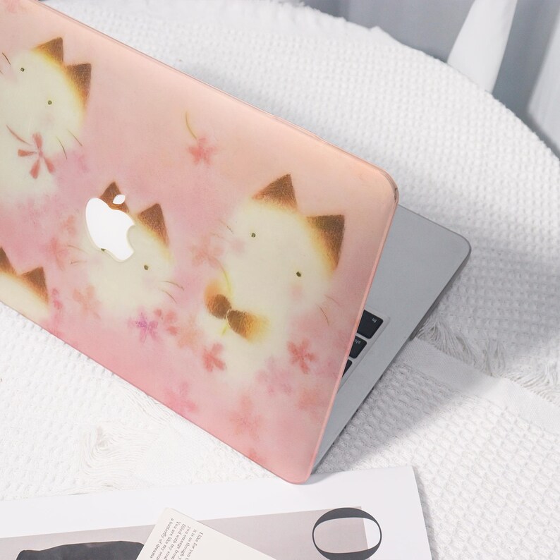 K&ouml;nnte beinhalten: Eine rosa Laptop-H&uuml;lle mit einem sich wiederholenden Muster von Cartoon-Katzen mit braunen Ohren und Fliegen sowie rosa Blumenakzenten. Das Apple-Logo ist sichtbar. Die H&uuml;lle befindet sich auf einem silbernen Laptop.