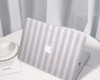 Może przedstawiać: Laptop z jasnoniebiesko-białą obudową w paski, z logo Apple. Laptop jest otwarty i leży na białej powierzchni, z białą filiżanką i spodkiem w tle. Całość ma czysty i minimalistyczny wygląd.