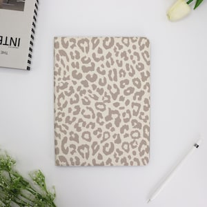 Peut inclure: Une couverture de carnet à motifs léopard beige et marron. La couverture est faite d'un matériau doux et durable avec un léger brillant.