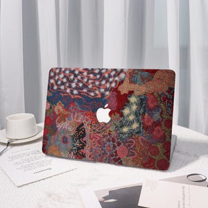 May include: A colorful laptop case featuring an abstract design with red, blue, and gold patterns. The case has a white Apple logo in the center. The design is reminiscent of a textile or painted artwork.