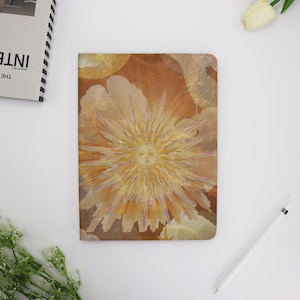 May include: A gold and brown notebook cover with a stylized sun design. The sun has a face and rays of light radiating from it.