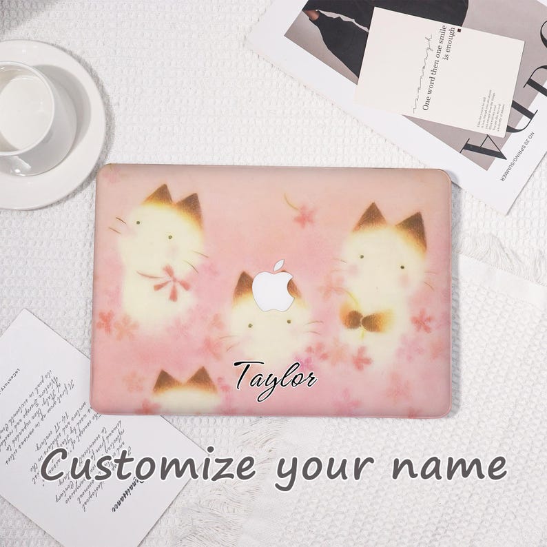 K&ouml;nnte beinhalten: Eine rosa Laptop-H&uuml;lle mit einem Muster aus Cartoon-Katzen mit braunen Ohren und Akzenten sowie floralen Details. Der Name "Taylor" und der Text "Customize your name" sind aufgedruckt.