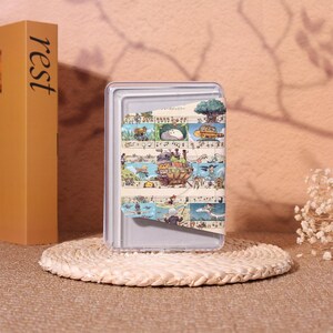 May include: A clear, rectangular phone case with a colorful illustration of a fantasy scene. The case is resting on a woven, circular coaster. A tan book with the word "rest" is visible.