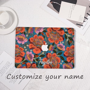 K&ouml;nnte beinhalten: Eine t&uuml;rkisfarbene Laptop-H&uuml;lle mit einem lebendigen Blumenmuster in Orange, Rosa und Gelb. Das Design enth&auml;lt den Namen "Taylor" in Schreibschrift und das Apple-Logo. Der Text "Customize your name" ist ebenfalls sichtbar.