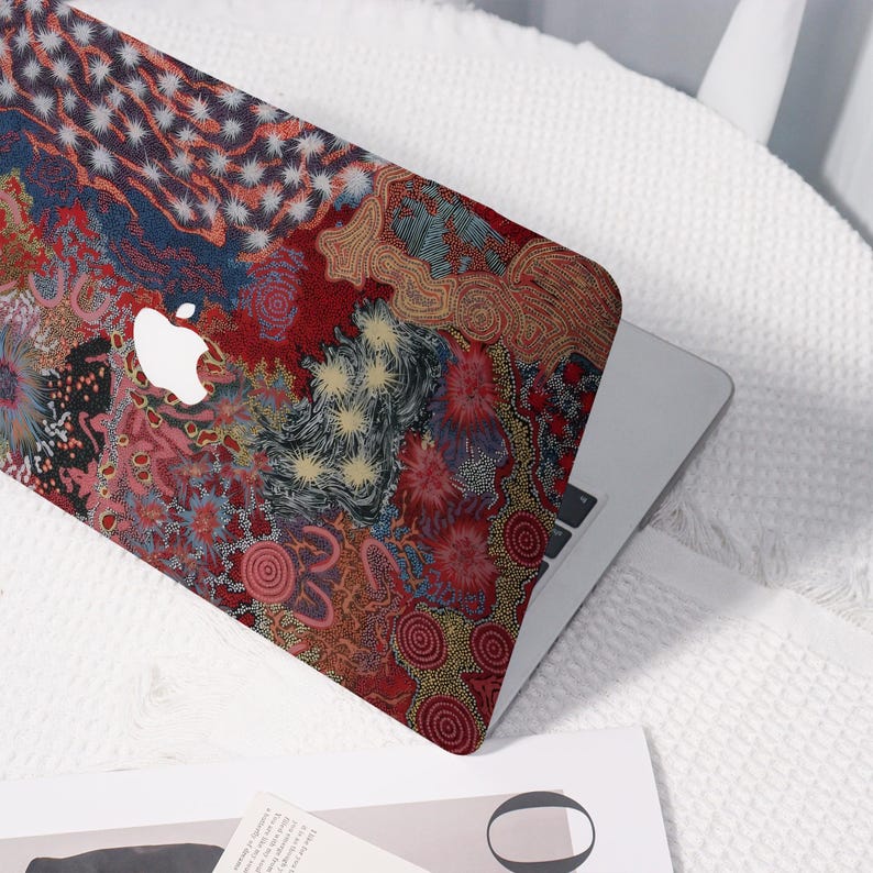 May include: A laptop with a colorful, patterned cover. The design features a mix of red, blue, and yellow abstract shapes and floral patterns. The Apple logo is visible on the cover.