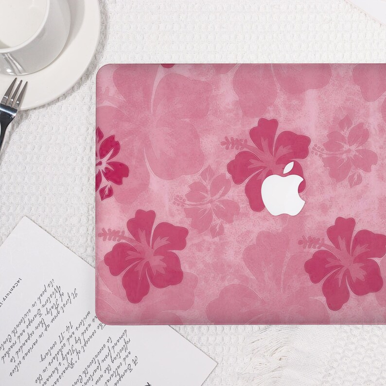 May include: Pink laptop case with a floral hibiscus pattern. The case features a white Apple logo and a textured background. The design includes various shades of pink, creating a vibrant and stylish look.