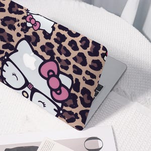 Pu&ograve; includere: Custodia per laptop con sfondo a stampa leopardata beige e un design di personaggi dei cartoni animati. Il design include un gatto bianco con un fiocco rosa e occhiali. Il laptop &egrave; argento.