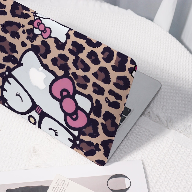 Pu&ograve; includere: Custodia per laptop con sfondo a stampa leopardata beige e un design di personaggi dei cartoni animati. Il design include un gatto bianco con un fiocco rosa e occhiali. Il laptop &egrave; argento.