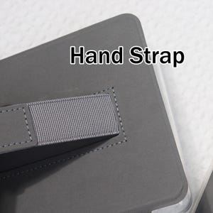 K&ouml;nnte beinhalten: Eine graue Tablettasche mit einer Handschlaufe. Der Text "Hand Strap" ist wei&szlig; auf der Tasche aufgedruckt. Die Handschlaufe besteht aus grauem Stoff und ist mit grauen N&auml;hten befestigt.