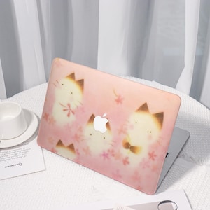 K&ouml;nnte beinhalten: Eine rosa Laptop-H&uuml;lle mit einem sich wiederholenden Muster von Cartoon-Katzen mit braunen Ohren und Akzenten sowie rosa floralen Elementen. Die H&uuml;lle hat ein wei&szlig;es Apple-Logo. Der Laptop befindet sich auf einer wei&szlig;en Oberfl&auml;che.