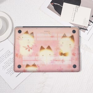 K&ouml;nnte beinhalten: Eine rosa MacBook Pro H&uuml;lle mit einem sich wiederholenden Muster von Cartoon-Katzen mit braunen Ohren und Akzenten. Die H&uuml;lle hat ein Blumenmuster und der Text "MacBook Pro" ist sichtbar.