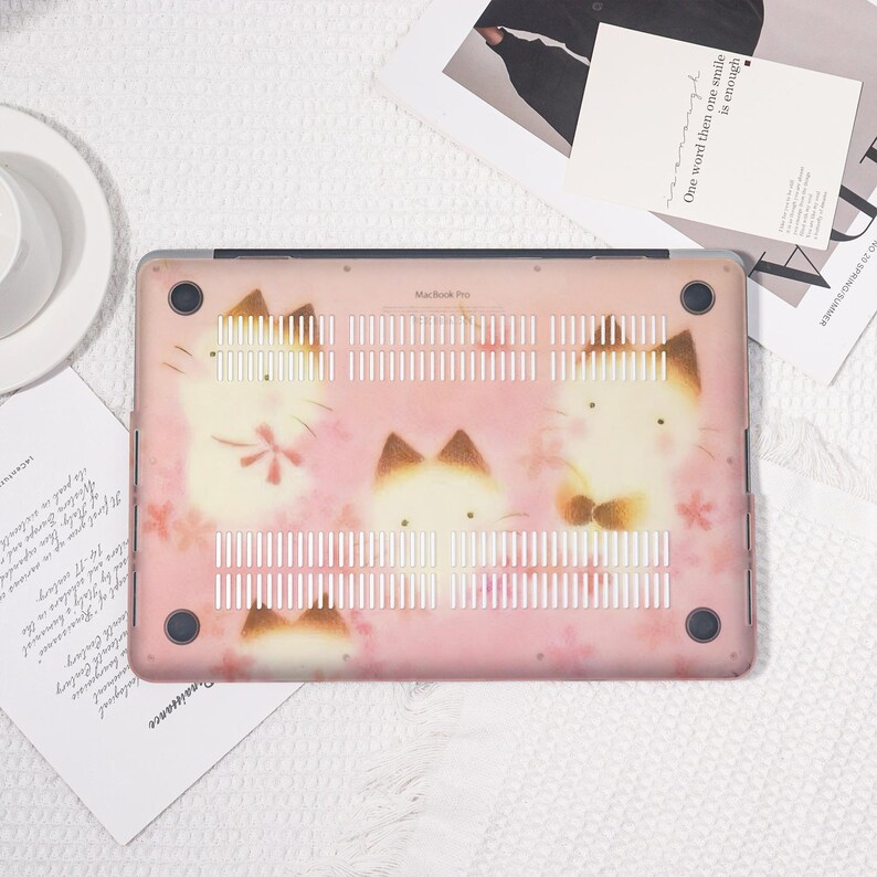 K&ouml;nnte beinhalten: Eine rosa MacBook Pro H&uuml;lle mit einem sich wiederholenden Muster von Cartoon-Katzen mit braunen Ohren und Akzenten. Die H&uuml;lle hat ein Blumenmuster und der Text "MacBook Pro" ist sichtbar.