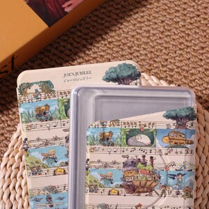 May include: A beige rectangular container with a clear lid. The container is decorated with a whimsical illustration featuring characters and scenes, with musical notes and the text "JOE'S JUBILEE" in English and Japanese.