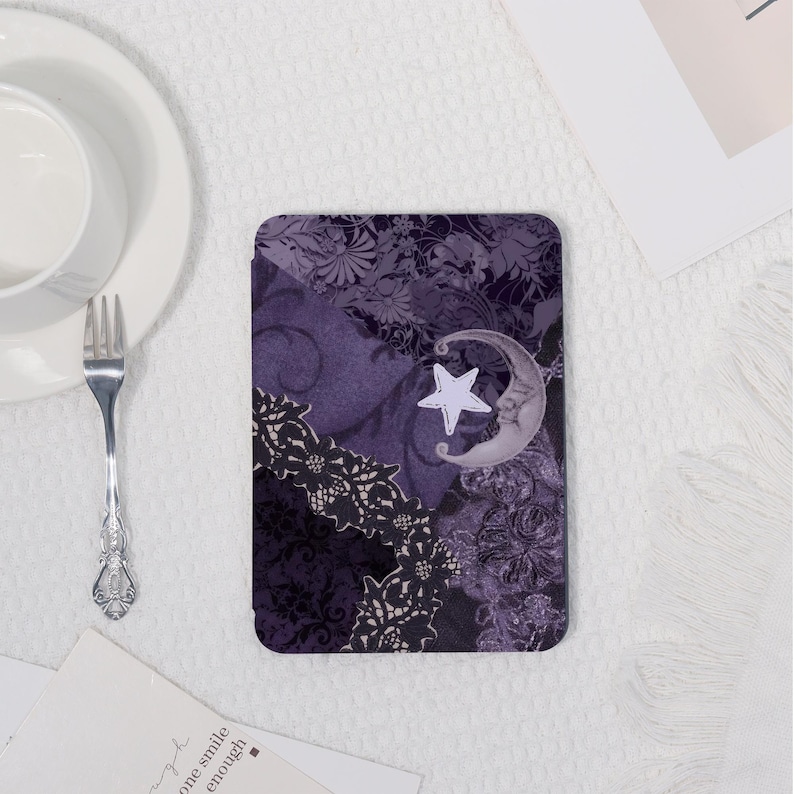 K&ouml;nnte beinhalten: Ein rechteckiger Untersetzer mit einem lila-schwarzen Blumenmuster, das einen Mond und einen Stern zeigt. Der Untersetzer hat ein dekoratives Spitzendesign und einen wei&szlig;en Stern. Der Hintergrund hat ein Blumenmuster.