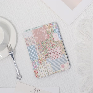 May include: A rectangular tablet case with a patchwork design. The case features a mix of floral and geometric patterns in pastel shades of pink, blue, and white. It is displayed on a white surface.