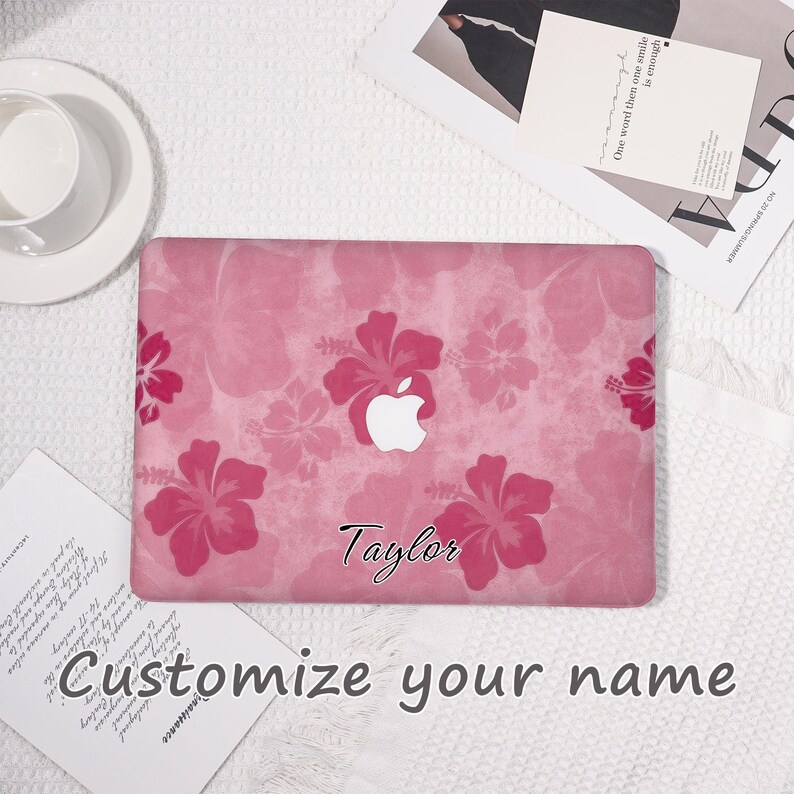 May include: A pink laptop case featuring a floral hibiscus pattern. The case has a white Apple logo and the name "Taylor" in cursive. The text "Customize your name" is also visible.