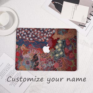 May include: A laptop cover with a colorful abstract design in red, blue, and gold. The cover features the Apple logo and the name "Taylor" in script. The text "Customize your name" is also visible.
