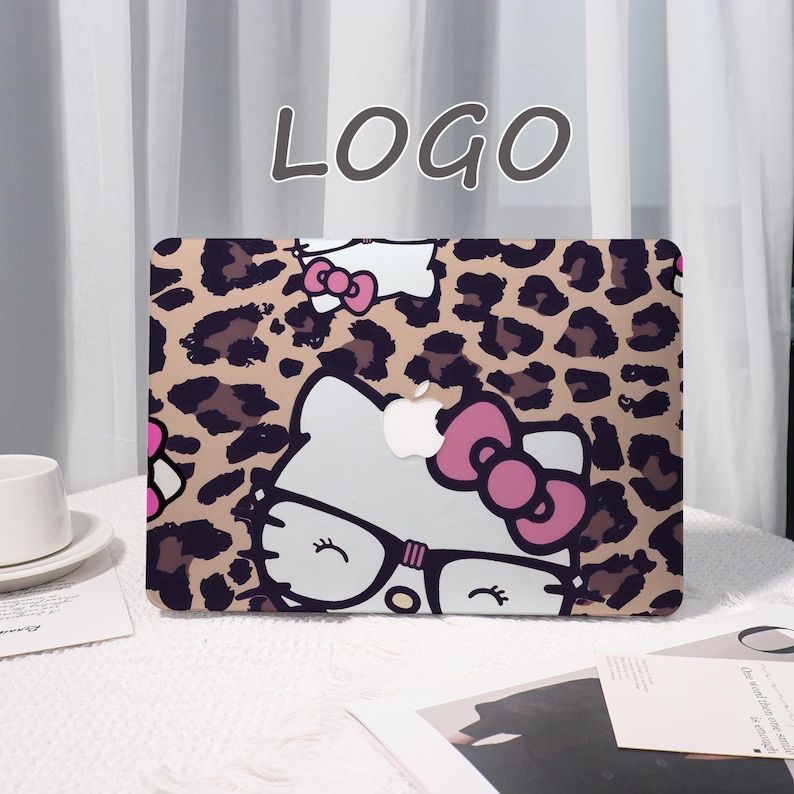 Pu&ograve; includere: Custodia per laptop con motivo leopardato e un personaggio di gatto dei cartoni animati con occhiali e fiocco rosa. La custodia ha un logo Apple bianco e la parola "LOGO" in alto al centro.
