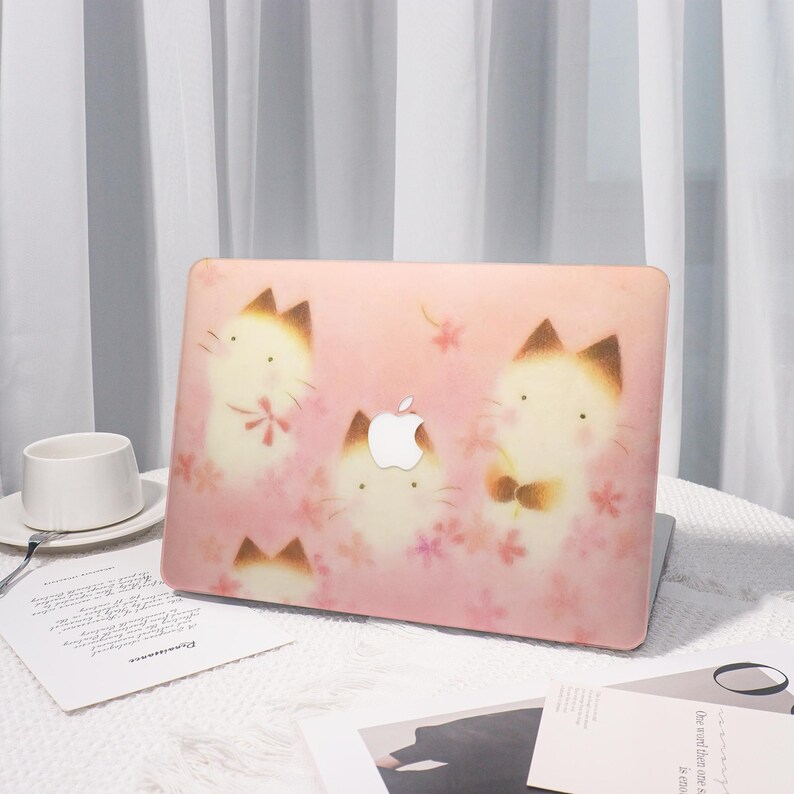 K&ouml;nnte beinhalten: Rosa Laptop-H&uuml;lle mit einem sich wiederholenden Muster aus Cartoon-Katzen und rosa Blumen. Die H&uuml;lle hat ein wei&szlig;es Apple-Logo und einen hellrosa Hintergrund. Die Katzen haben braune Ohren und tragen Schleifen.