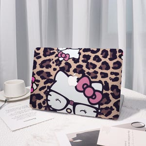Pu&ograve; includere: Una custodia per laptop con un motivo leopardato e un personaggio di gatto dei cartoni animati con occhiali e un fiocco rosa. La custodia &egrave; beige con macchie marroni e un volto di gatto bianco con dettagli neri.