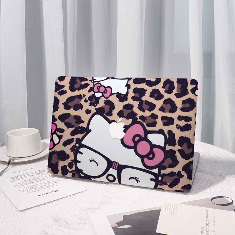 Pu&ograve; includere: Una custodia per laptop con un motivo leopardato e un personaggio di gatto dei cartoni animati con occhiali e un fiocco rosa. La custodia &egrave; beige con macchie marroni e un volto di gatto bianco con dettagli neri.