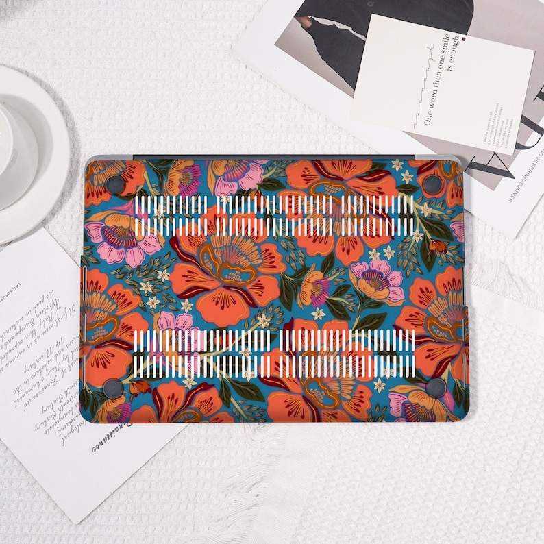 K&ouml;nnte beinhalten: Eine Laptop-H&uuml;lle mit einem lebendigen Blumenmuster. Die H&uuml;lle zeigt gro&szlig;e orangefarbene und rosa Bl&uuml;ten mit gr&uuml;nen Bl&auml;ttern und wei&szlig;en Akzenten auf einem t&uuml;rkisfarbenen Hintergrund. Die H&uuml;lle hat eine Reihe wei&szlig;er vertikaler Linien.