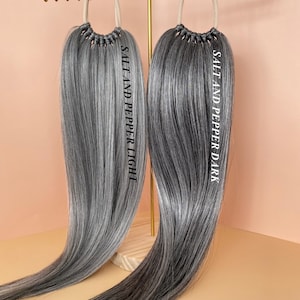 May include: Two long, straight hair extensions in a salt and pepper color. The extension on the left is labeled "Salt and Pepper Light" and the extension on the right is labeled "Salt and Pepper Dark".
