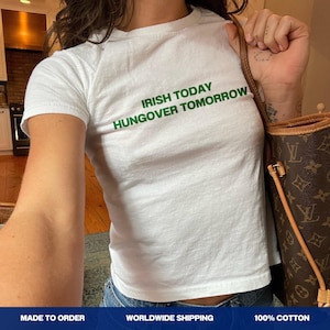May include: White t-shirt with the green text "IRISH TODAY HUNGOVER TOMORROW". The shirt is a crew neck style and appears to be made of cotton. The shirt is being worn.