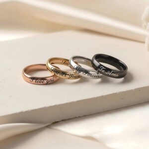 Peut inclure: Un ensemble de quatre bagues en m&eacute;tal lisse aux tons or rose, or, argent et noir. Chaque bague pr&eacute;sente une finition polie et est grav&eacute;e d'une inscription en &eacute;criture cursive incluant les phrases I love you, Forever Yours, My Forever et Te Amo.