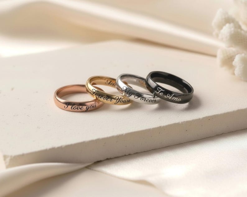 Peut inclure: Un ensemble de quatre bagues en m&eacute;tal lisse aux tons or rose, or, argent et noir. Chaque bague pr&eacute;sente une finition polie et est grav&eacute;e d'une inscription en &eacute;criture cursive incluant les phrases I love you, Forever Yours, My Forever et Te Amo.