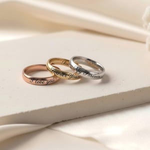 Peut inclure: Trois bagues en m&eacute;tal aux tons or rose, or jaune et argent. Chaque bague pr&eacute;sente un anneau lisse et arrondi avec un texte grav&eacute; en noir. La bague en or rose porte l'inscription I love you, celle en or jaune Forever Yours et l'argent&eacute;e My Forever.
