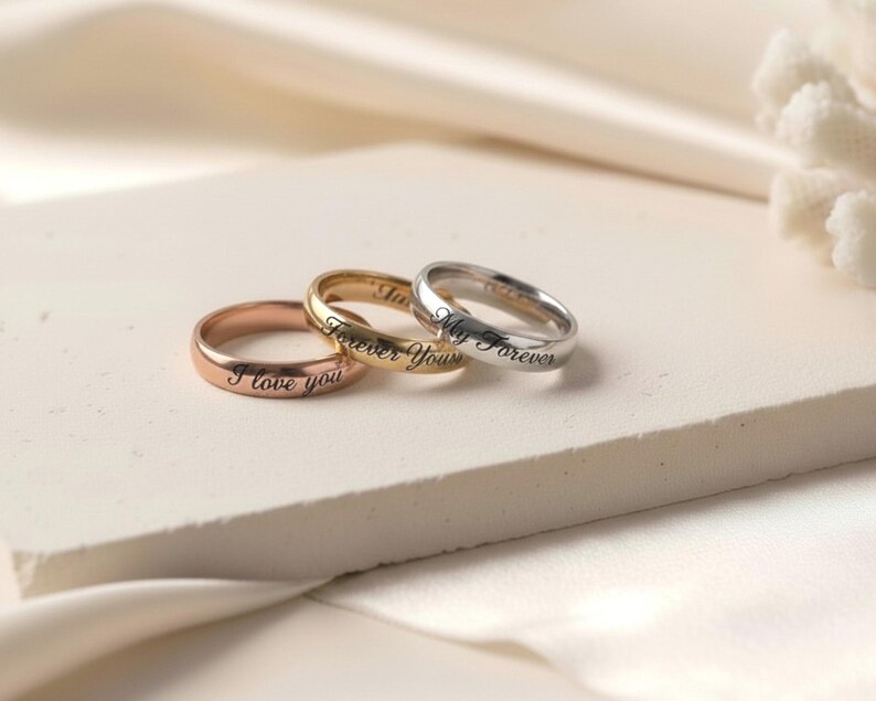 Peut inclure: Trois bagues en m&eacute;tal aux tons or rose, or jaune et argent. Chaque bague pr&eacute;sente un anneau lisse et arrondi avec un texte grav&eacute; en noir. La bague en or rose porte l'inscription I love you, celle en or jaune Forever Yours et l'argent&eacute;e My Forever.
