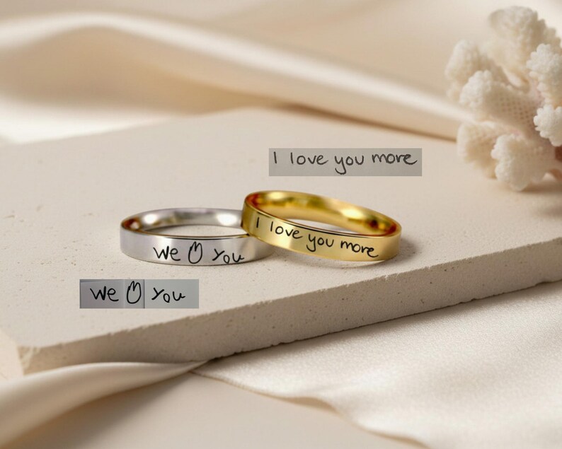 Peut inclure: Deux bagues en m&eacute;tal, une argent&eacute;e et une dor&eacute;e, chacune pr&eacute;sentant une gravure manuscrite. La bague argent&eacute;e porte l'inscription "we [symbole c&oelig;ur] you" et la bague dor&eacute;e porte l'inscription "I love you more."