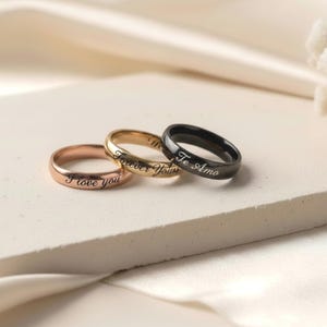 Peut inclure: Trois bagues en m&eacute;tal aux tons or rose, or et noir. Chaque anneau pr&eacute;sente une finition lisse et polie avec une gravure en &eacute;criture cursive. La bague en or rose porte l'inscription I love you, celle en or Forever Yours et la noire Te Amo.