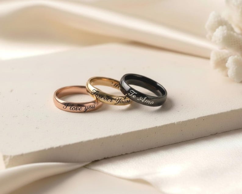 Peut inclure: Trois bagues en m&eacute;tal aux tons or rose, or et noir. Chaque anneau pr&eacute;sente une finition lisse et polie avec une gravure en &eacute;criture cursive. La bague en or rose porte l'inscription I love you, celle en or Forever Yours et la noire Te Amo.